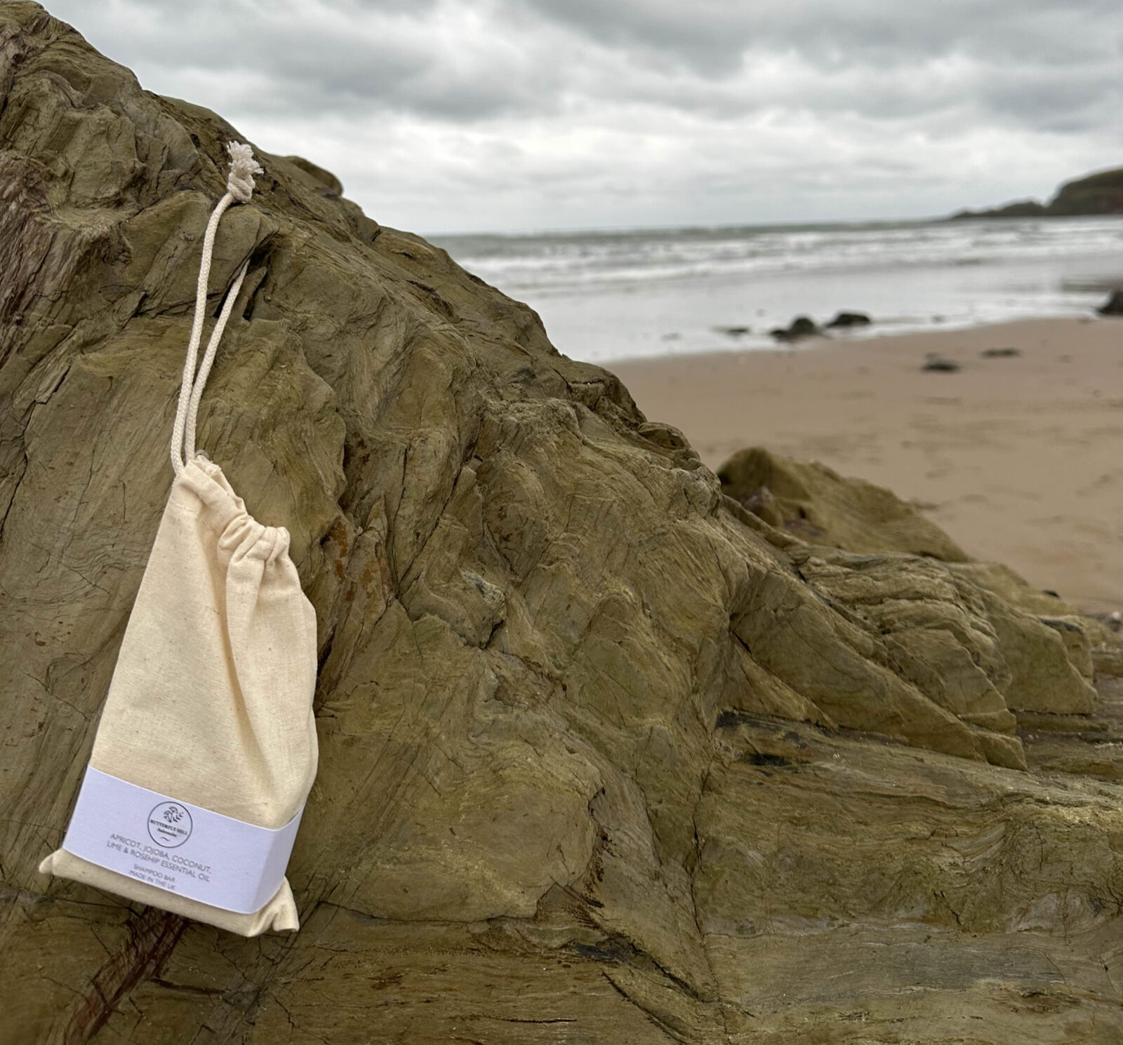 Butterfly Hill shampoo bar in a cotton bag on the rocks by the sea
