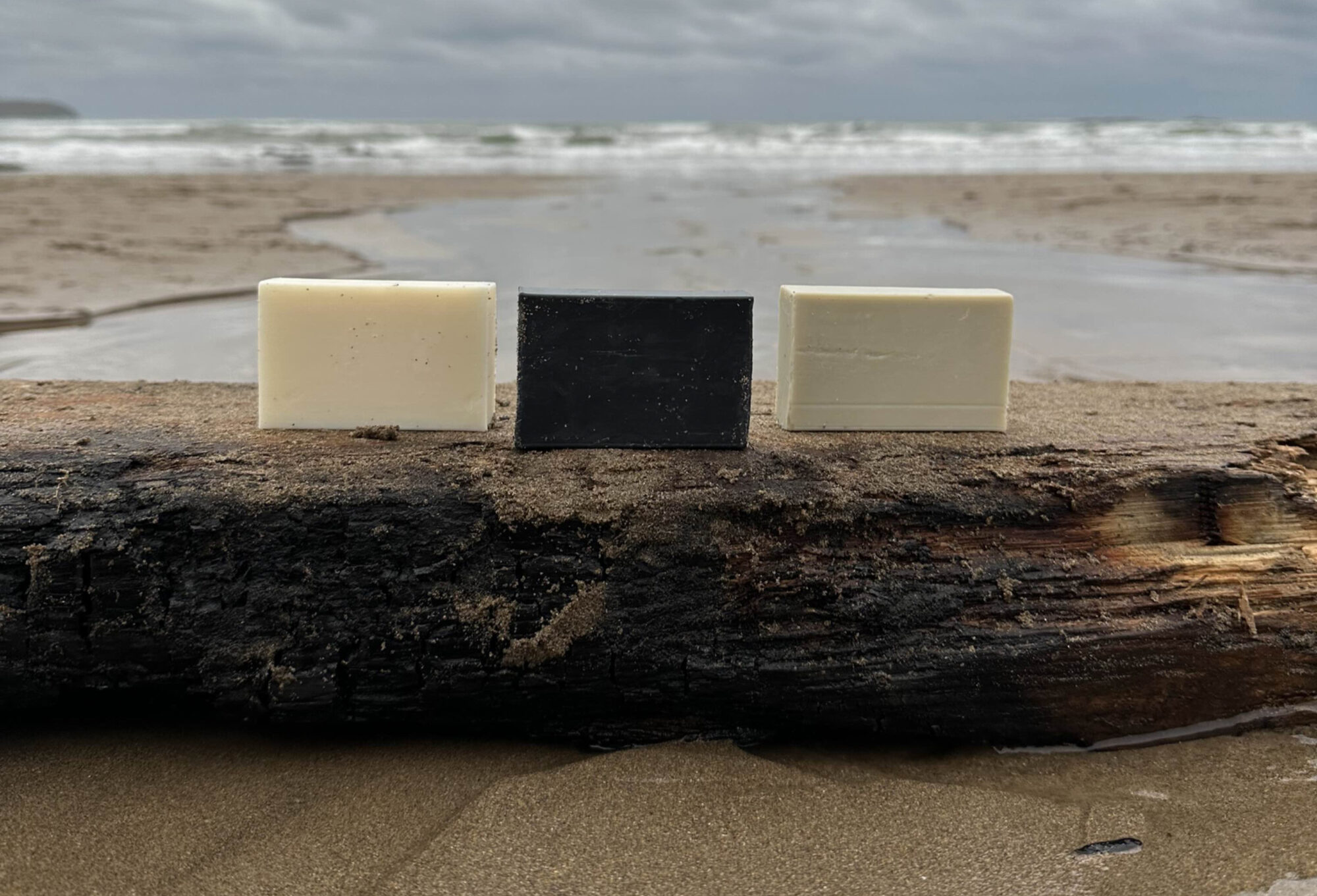 Three Butterfly Hill soap bars on driftwood by the sea
